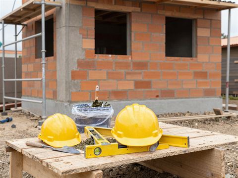Obra de construcción de ladrillo con cascos amarillos y herramientas